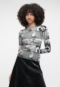 Μακρυμάνικο τοπ με ασπρόμαυρη κομικ εκτύπωση, κατασκευασμένο από ανοιχτό ύφασμα. Συνδυάζεται με μια υφασμάτινη μαύρη φούστα.