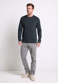 Mörkgrön långärmad t-shirt med rund hals; ihop med ljusgrå byxor och beige sneakers; minimal textur och detalj.