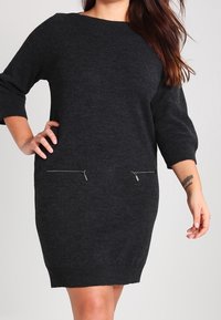 Robe en tricot gris foncé avec manches trois-quarts, encolure arrondie et deux poches avant zippées. Texture lisse et coupe ajustée.