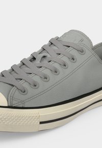 Γκρι δερμάτινο χαμηλό sneaker με ταιριαστά κορδόνια, λευκή λαστιχένια σόλα με μαύρη ρίγα και υφή στο μπροστινό μέρος, εμφανίζεται από πλάγια γωνία.