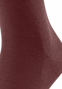 Chaussette bordeaux avec une texture lisse, un design côtelé et un talon renforcé. La vue rapprochée montre un rétrécissement progressif et des coutures uniformes.