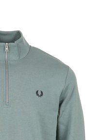 Maglione con mezza cerniera in tessuto morbido color teal tenue. Presenta un piccolo logo scuro sul petto a sinistra e una robusta cerniera argentata.
