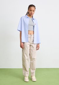 Light blue short-sleeve shirt over a gray crop top, paired with beige wide-leg pants and cream sneakers on a green floor.