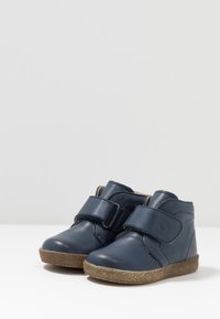 Stivaletti in pelle blu navy con cinturino in velcro, punta arrotondata e suola in gomma marrone texturizzata. Finitura liscia con dettagli cuciti.