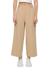 Beige wijde broek met een op maat gemaakte hoge taille, voorzien van twee knopen en plooien, gemaakt van een gladde, lichte stof. Gecombineerd met witte sneakers.