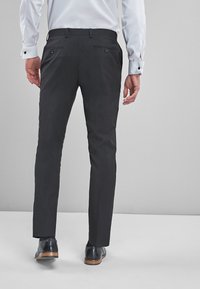 Pantaloni negri, cretați pe măsură, cu o croială slim, având două buzunare la spate și un material neted. Purtați cu o cămașă albă și pantofi dark.