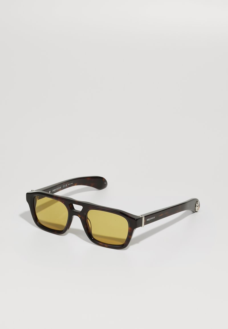 Ochelari de soare rectangulari cu rame din material tortoise și lentile galbene. Prezintă accente argintii și un finisaj texturat pe brațe.