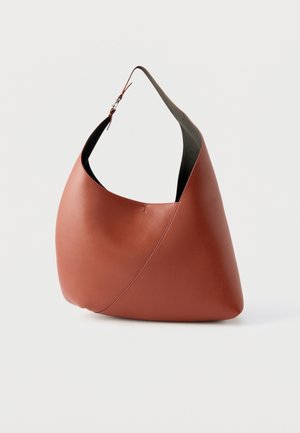 Sac à bandoulière en cuir marron avec un design incurvé et asymétrique et une sangle ajustable, sur fond blanc uni.