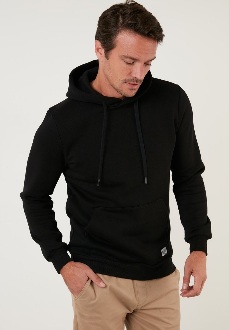 Sudadera negra hecha de un tejido suave y elástico. Cuenta con un gran bolsillo frontal, cordones ajustables y puños acanalados.