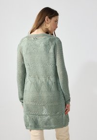 Μακρυμάνικο ανοιχτό πλεκτό κα cardigan σε α�παλό μέντα, με γεωμετρικά σχέδια και υφή, χαλαρή εφαρμογή και πλευρικές σχισμές.