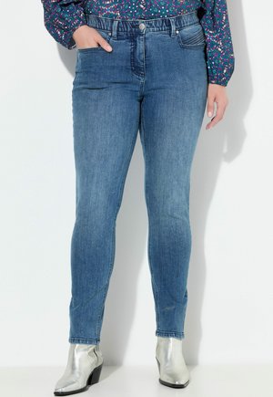 Jeans skinny blu in denim, con vita alta, tasche frontali e una texture liscia. Abbinati a stivaletti metallici argento alla caviglia.