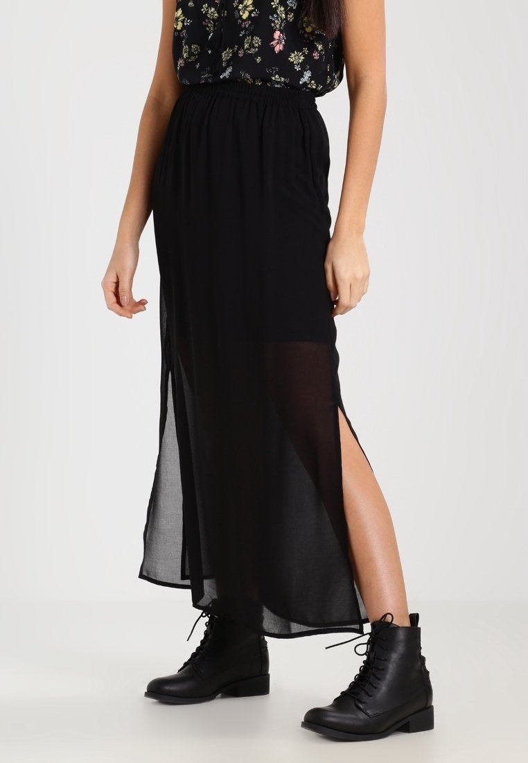 Jupe longue en chiffon noir avec fentes latérales hautes, taille élastique, associée à des bottines noires à lacets. Design léger et fluide.