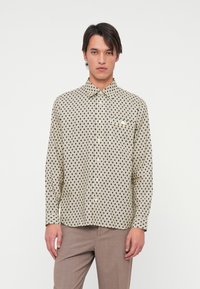 Langarm overhemd in crème met een zwart geometrisch patroon, kraag en een enkele borstzak. De stof lijkt glad en lichtgewicht.