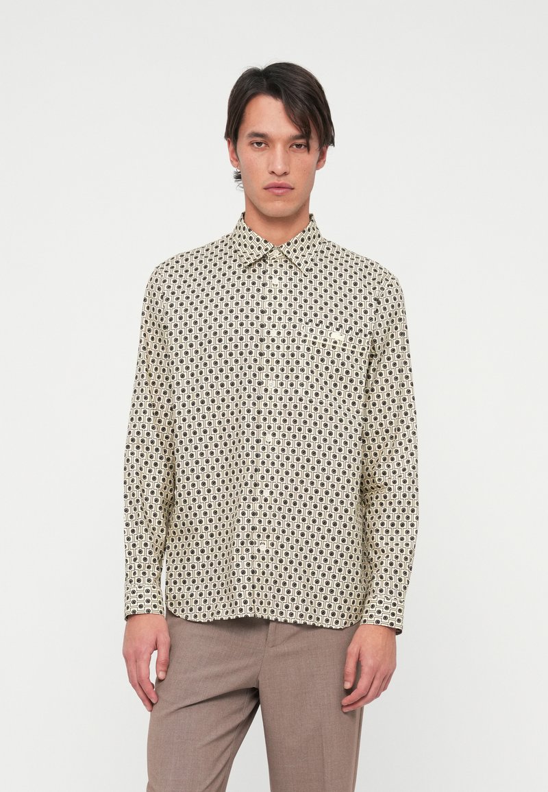 Langarm overhemd in crème met een zwart geometrisch patroon, kraag en een enkele borstzak. De stof lijkt glad en lichtgewicht.