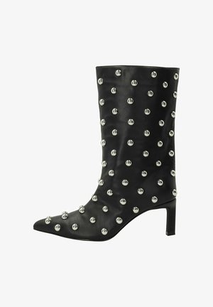 Bottine en cuir noir avec un bout pointu, ornée de clous ronds en argent disposés en motif sur la surface et à talon bas carré.