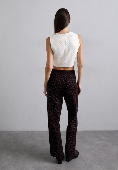 Witte cropped top met kleine zwarte stippen, gecombineerd met bruine wijde broek met witte stippen. Glad textuur, minimalistisch ontwerp.