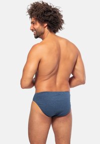 Blauwe gestreepte zwemslips van gladde stof, met een nauwsluitende pasvorm en een lage taille. Het model is van achteren te zien.
