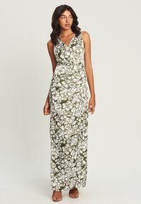 Maxi dress in white with green floral pattern, featuring a v-neck, sleeveless design, and a fitted waist that flows to a floor-length hem.