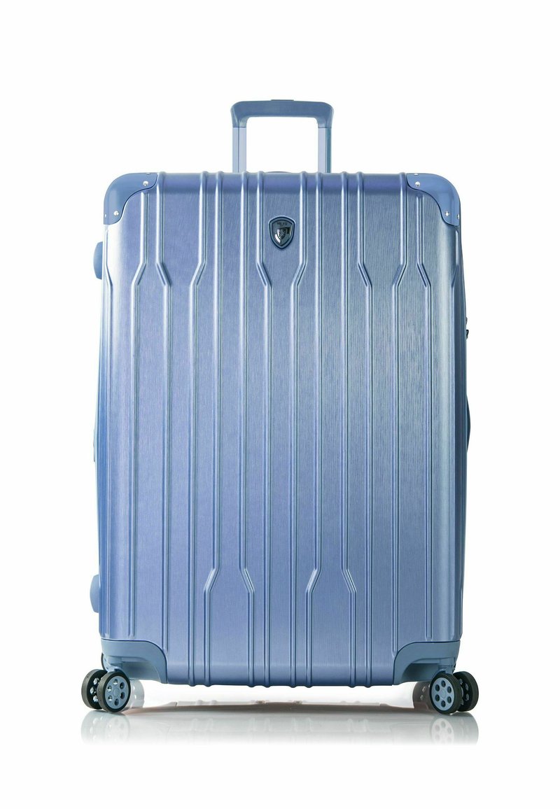 Hartschalenkoffer aus hellblauem Aluminium mit vertikalen Rillen, vier Rädern und einem ausziehbaren Griff. Mit einem Logo auf der Vorderseite.