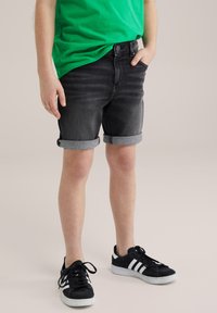 Črni jeans kratke hlače s zavihanimi robovi, z klasičnim pet-žepnim dizajnom. Kombinirane s črnimi supergami in zeleno majico.
