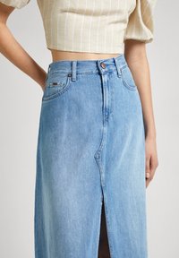 Light blue denim skirt with a front slit, high waist, and classic five-pocket design. Features copper-tone button and zipper closure.