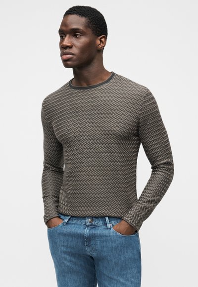 Camisa de manga comprida castanha com padrão em zigzag, decote arredondado e corte justo, combinada com calças de ganga azuis.