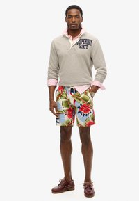 Jasnoszara longsleeve polo z granatowym nadrukiem, nałożony na różową koszulę; wielokolorowe kwiatowe kąpielówki; burgundowe buty żeglarskie.