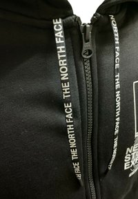 Felpa con zip nera realizzata in tessuto morbido, con cordini bianchi a contrasto e la scritta "THE NORTH FACE" stampata più volte.