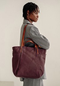 Borsa tote viola, robusta, con manici in pelle, dotata di tasche esterne e logo impresso sul lato. Texture liscia, design spazioso.