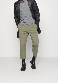 Szary polo, czarna skórzana kurtka, dopasowane oliwkowe spodnie oraz czarne botki za kostkę o gładkim wykończeniu i kontrastowym przeszyciu.