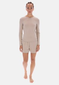 Conjunto beige de top de manga larga y pantalones cortos a juego confeccionados en tela suave, que presenta un cuello redondo y cintura elástica, utilizado descalzo.