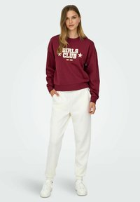 Burgundy sweatshirt with "GIRLS CLUB" text and stars, paired with white fleece joggers and white sneakers, showcasing a casual outfit.