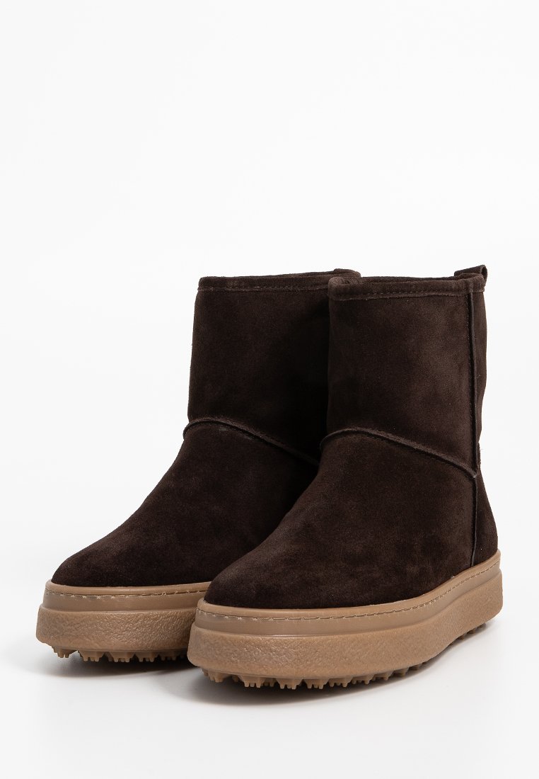 Braune Wildleder-Stiefel mit flacher, strukturiertem Sohle und minimalen Nähakzenten. Sie zeichnen sich durch eine glatte, runde Form und ein mittelhohes Design aus.