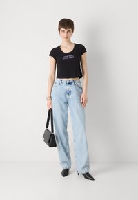 Crni skraćeni majica s izvezenim "Calvin Klein od 1968.", svijetloplave široke traperice, crne štikle na špic, i mala crna torbica.