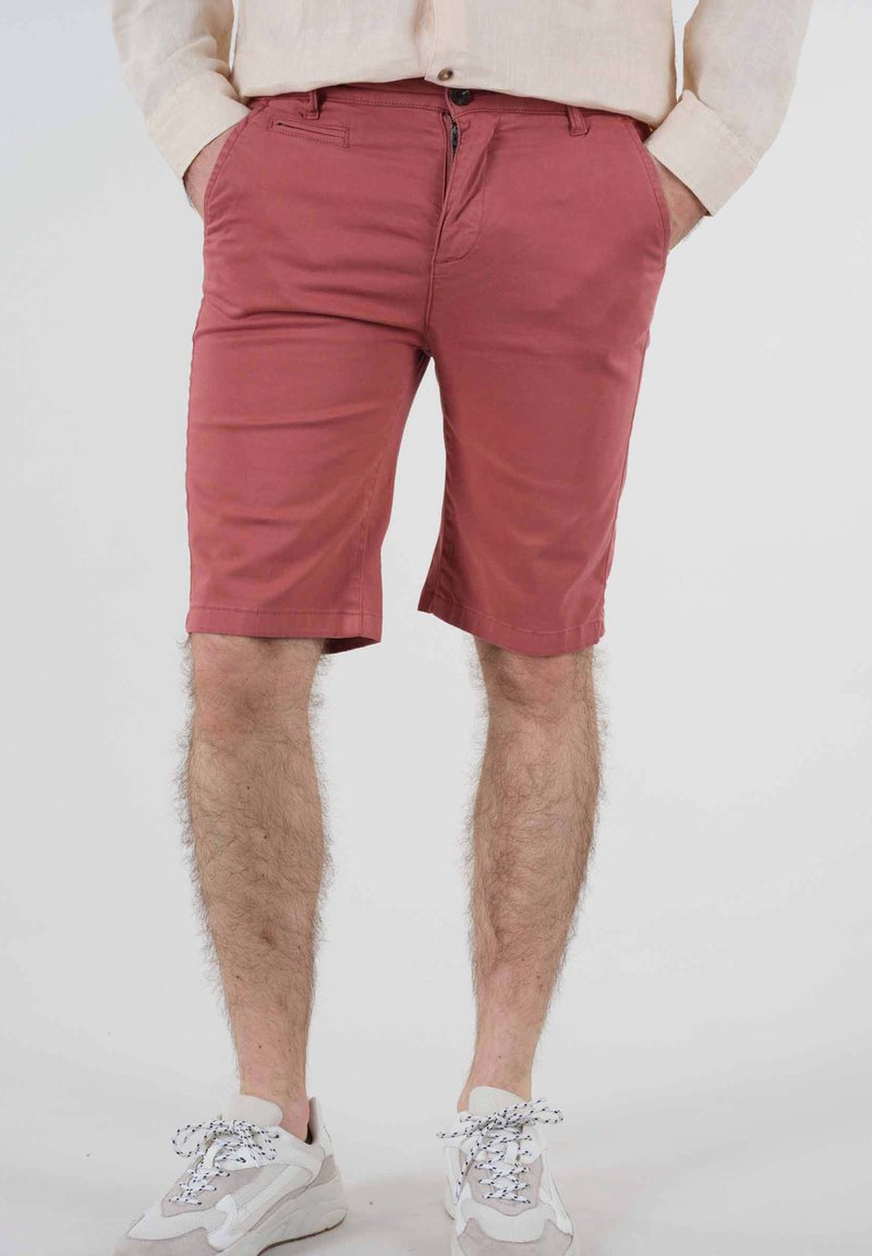 Shorts en coton rose avec une coupe slim, poches standards et braguette zippée. Associés à des baskets grises et blanches avec des lacets à motifs.