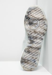 Sneaker med texturerad sula, ljusgrön ovandel och en vit detalj. Har en cirkulär logotyp och ett hexagonalt mönster på yttersulan.