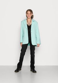 Blazer oversized azul claro com lapelas em bico, combinado com uma blusa preta e calças pretas, usado com sapatos pretos. Textura lisa, corte descontraído.