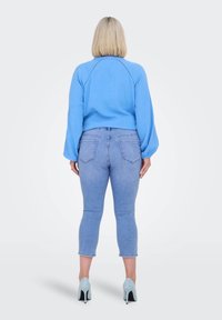 Suéter corto de color azul claro con mangas caídas, combinado con jeans azul claro y zapatos de tacón azul claro, visto desde atrás.