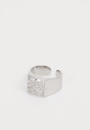 Anillo abierto de plata con una cara cuadrada irregular y texturizada sobre un fondo blanco liso.