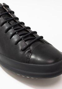 Mustmust mustrepp nahkaring, ümmarguse ninaga, lame kummitald ja mustad sidemed. Iseloomustab minimaalne õmblemine ja sile tekstuur.