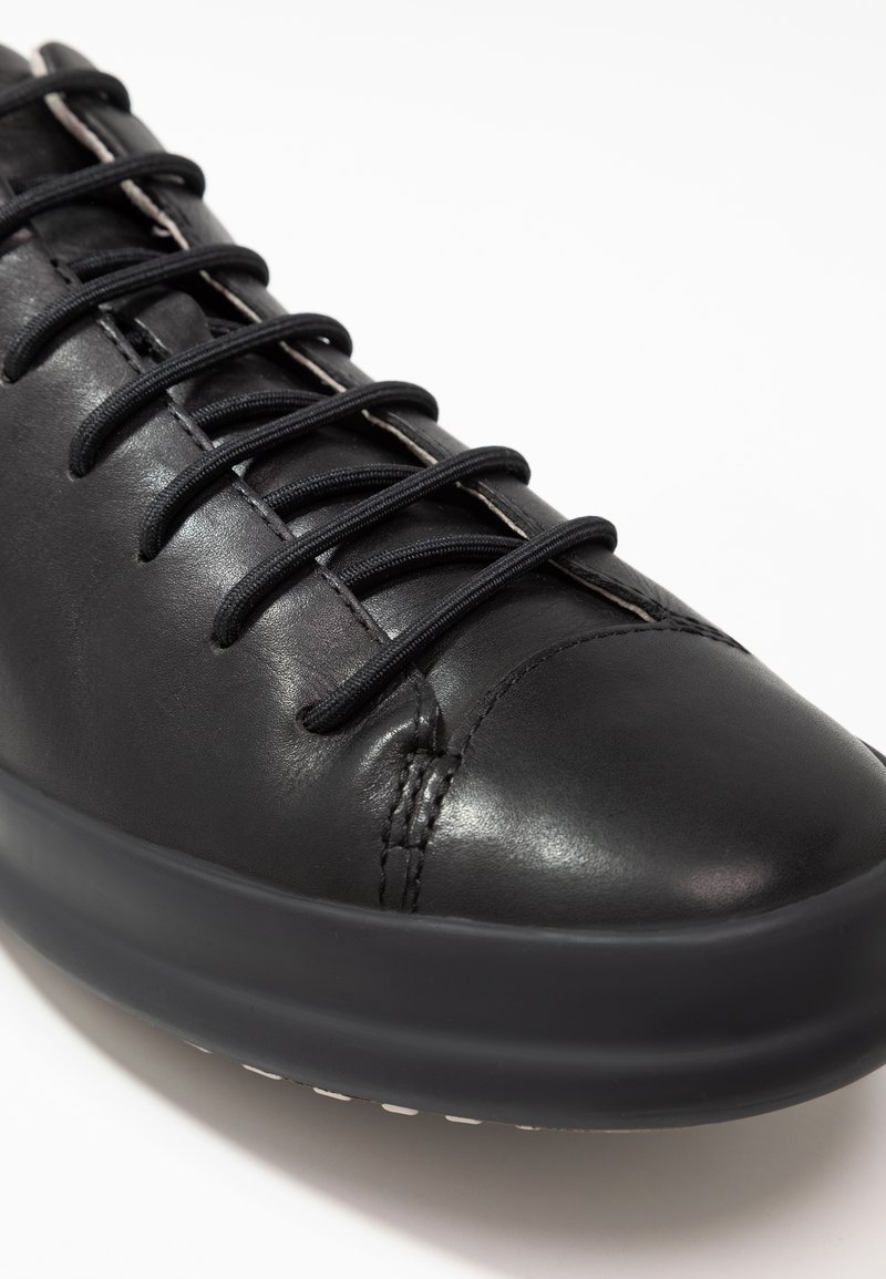 Schwarze Leder-Sneaker mit runder Zehenpartie, flacher Gummisohle und schwarzen Schnürsenkeln. Verfügt über minimale Nähte und eine glatte Textur.