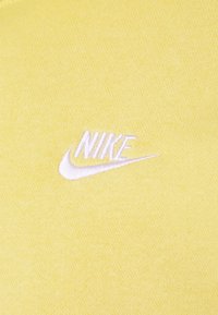 Gult bomullstyg med en slät struktur har en vit broderad Nike-logotyp på vänster sida.