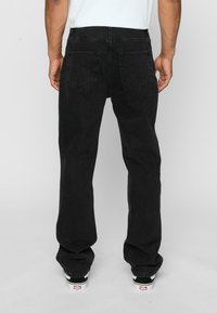 Jeans negre din denim cu croială drept, având două buzunare posterior și un brau clasic. Purtați cu adidași negri și albi.