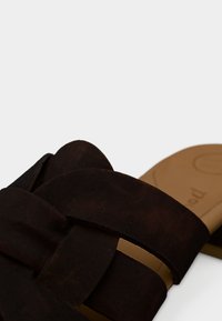 Sandales marron foncé à enfiler en daim souple. Dotées de larges brides croisées, d'une semelle intérieure rembourrée et d'un design de semelle simple.