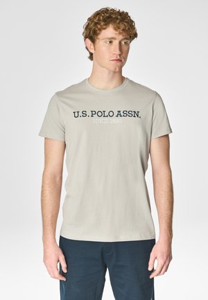 T-shirt grigio chiaro con collo a giro, con la scritta "U.S. POLO ASSN." stampata in blu navy sul petto. Materiale in morbido cotone misto.
