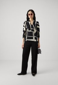 Blusa a maniche tre quarti nera e crema a fantasia, abbinata a pantaloni neri a gamba larga e décolleté neri a punta. Piccola borsa grigia.