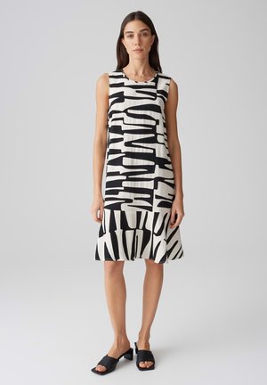 Robe sans manches avec un motif abstrait noir et blanc, dotée d'un col rond et d'un ourlet évasé. Associée à des sandales à talons carrés noires.