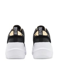 Baskets noires et dorées avec une tige texturée, une semelle épaisse blanche et un logo sur la languette et le talon. Des accents réfléchissants mettent en valeur le design.