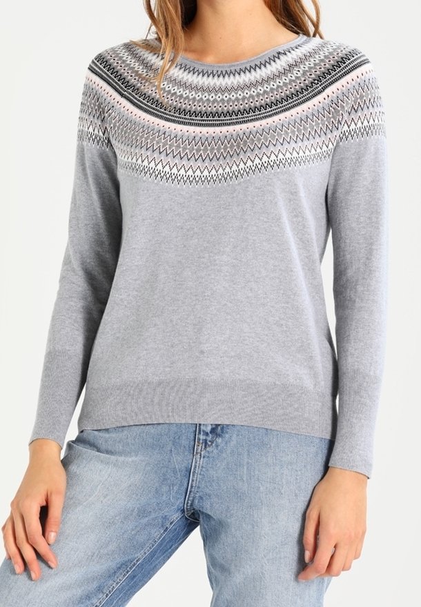 Pull gris clair avec un col rond, présentant un motif en zigzag noir, blanc et rose sur la poitrine et les épaules, porté avec un jean bleu.