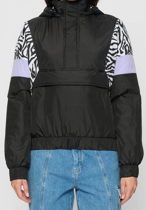 Black hooded jacket with zebra print and lavender panels on sleeves worn with blue jeans, front view from mid-thigh up.